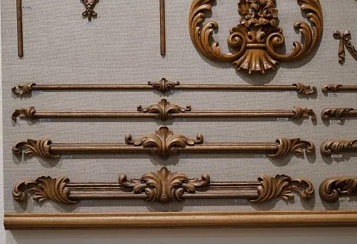 Резные деревянные декоративные элементы разной длины и формы, аккуратно размещённые на стенде, демонстрирующие богатство фактур и стилей.