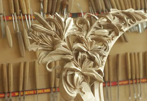 Резной элемент из дуба с изысканным цветочным орнаментом, выполненный вручную, на фоне мастерских инструментов.