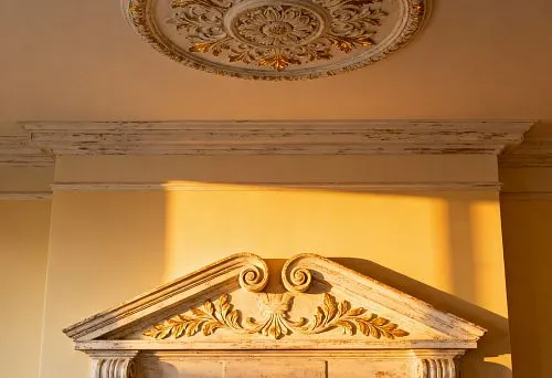 Потолочная розетка с позолотой и резной фронтон камина в классическом интерьере