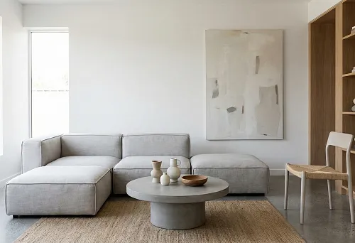 Минималистичная гостиная с серым модульным диваном, круглым бетонным журнальным столом, джутовым ковром и абстрактной картиной