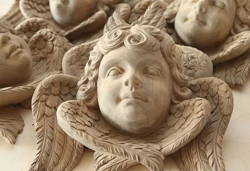 Резная скульптура головы ангела с крыльями, выполненная вручную из дуба, с детальной проработкой лица и перьев.