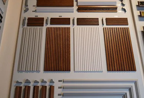 Коллекция настенных декоративных панелей и молдингов в различных оттенках и профилях, выстроенных на стенде. 