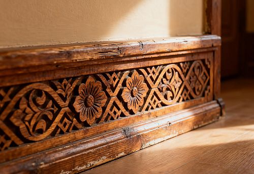 Резной деревянный плинтус с орнаментом в русском стиле на фоне тёплого пола из натурального дерева