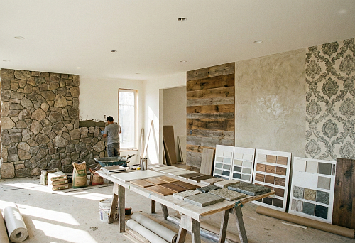 Рабочий укладывает декоративный камень на стену в частном доме.