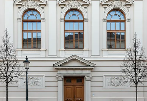 Фасад классического здания со средниками, сандриками и декоративными обрамлениями над окнами и дверью