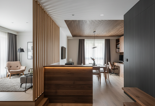 Интерьер с зонированием с помощью деревянных реек, панелей и погонажа, разделяющих пространство гостиной, кухни и рабочей зоны.