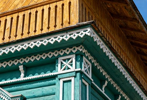 Теремной фасад деревянного дома с резными белыми наличниками, рейками и угловыми элементами на фоне зелёного сруба