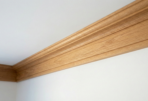Широкий потолочный деревянный карниз с плавным профилем на стыке стены и белого потолка